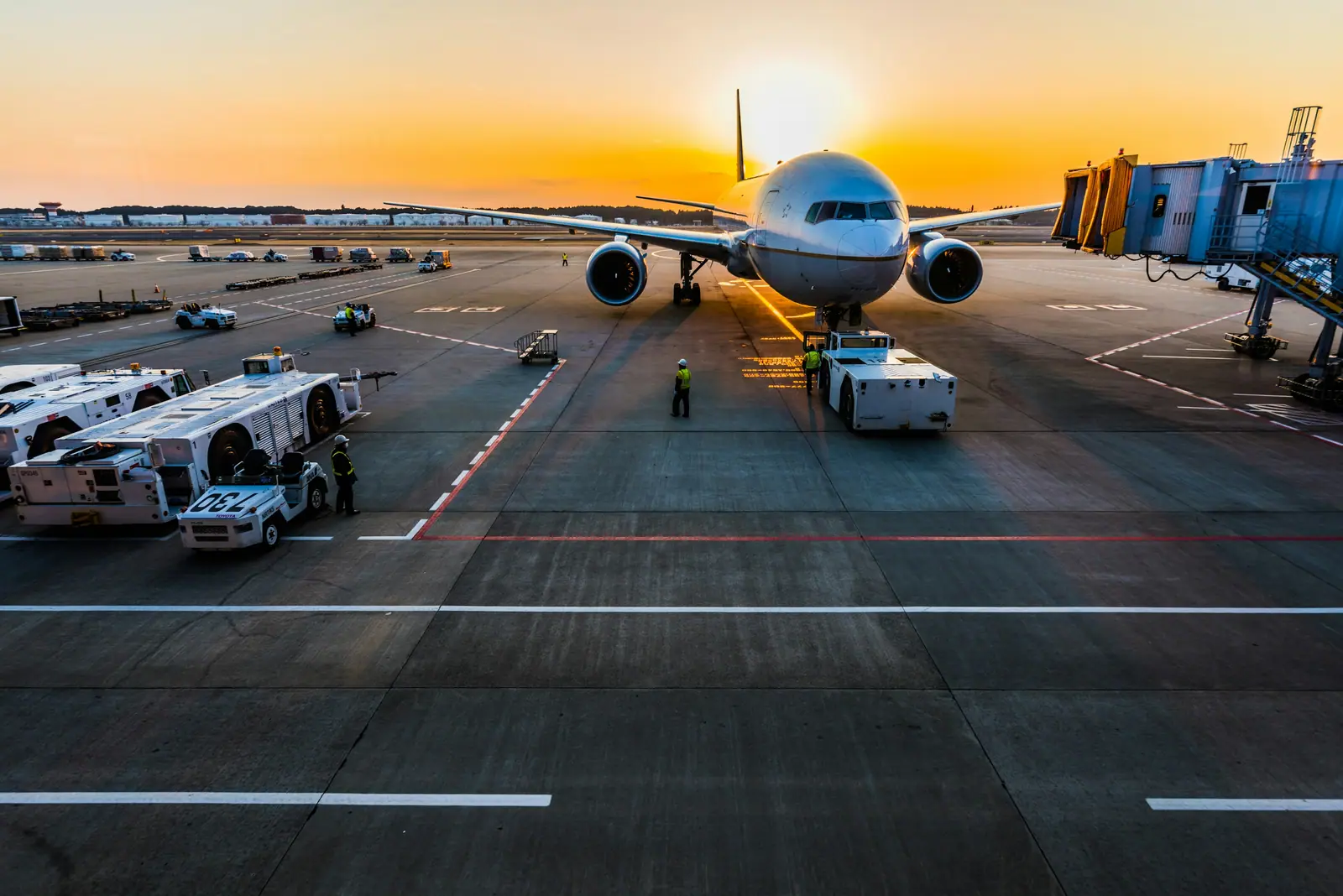 Wide-body aircraft on the apron at sunset with ground handling vehicles alongside
