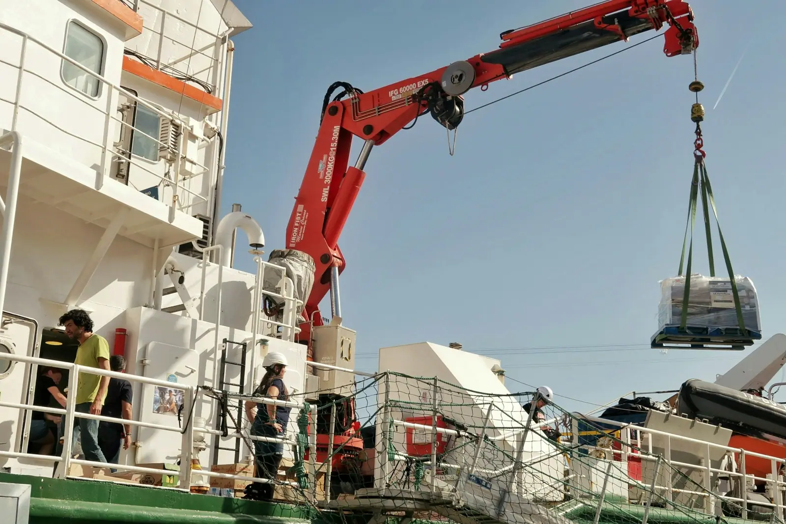 Ship crane lifting a slung palletised load on board a vessel