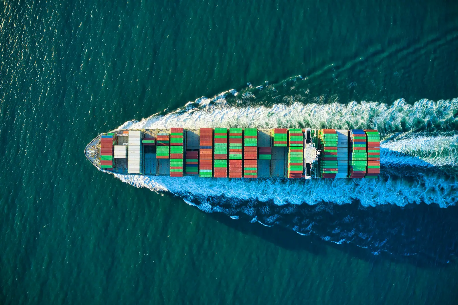 Container ship cutting a white wake through the open sea, seen from above