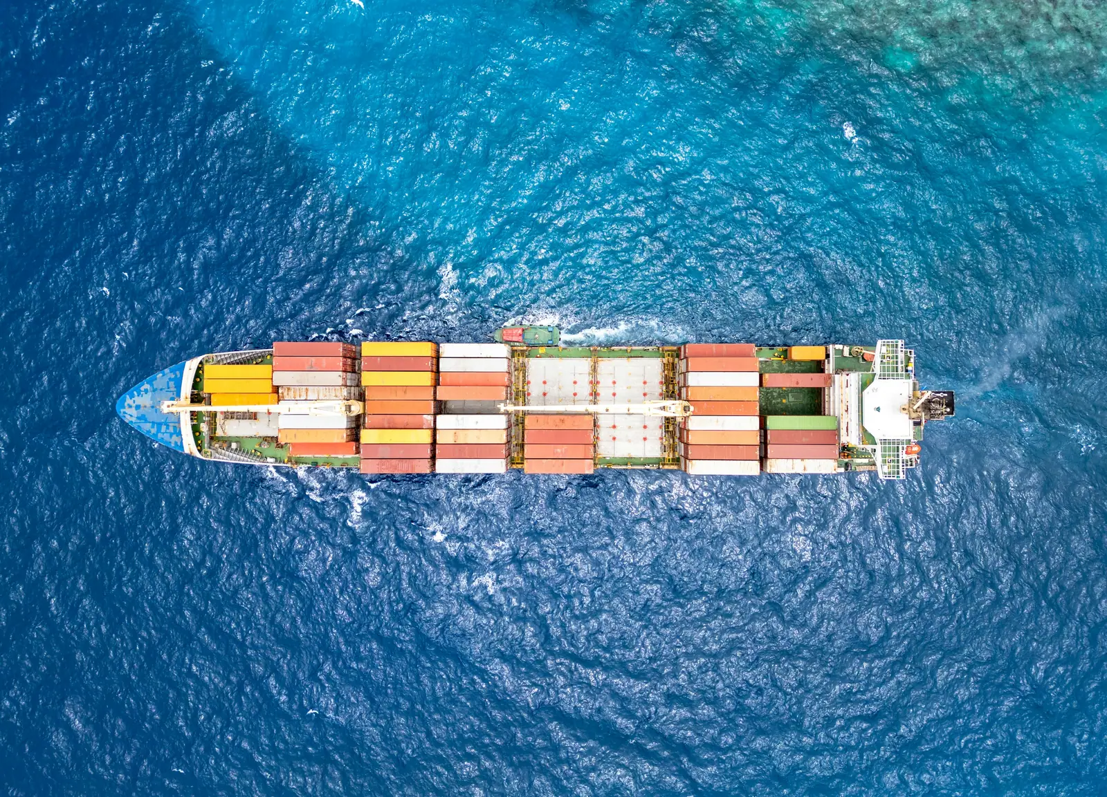 Container ship under way on bright blue water, seen from above