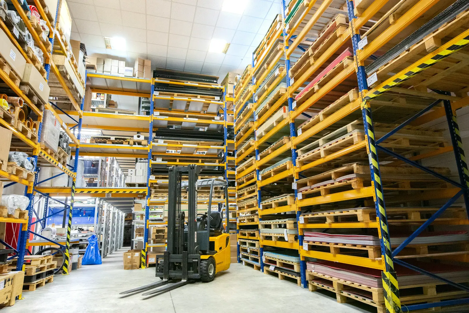 Warehouse aisle with pallets stacked high on yellow racking and a forklift in the centre